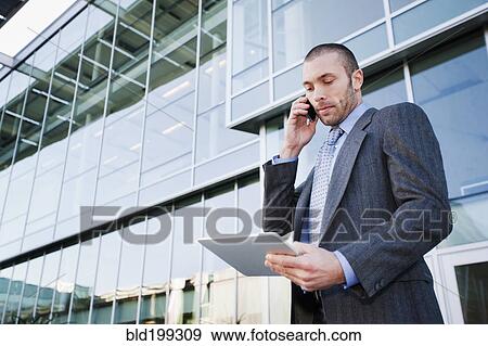 Stock Photo - Businessman using cell phone and digital tablet outdoors. Fotosearch