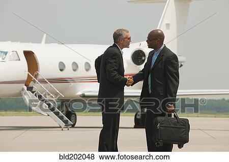Businessmen shaking hands on airport tarmac View Large Photo Image Stock Photo - Businessmen shaking hands on airport tarmac. Fotosearch