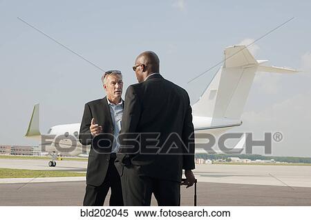 Stock Photography - Businessmen standing on airport tarmac. Fotosearch