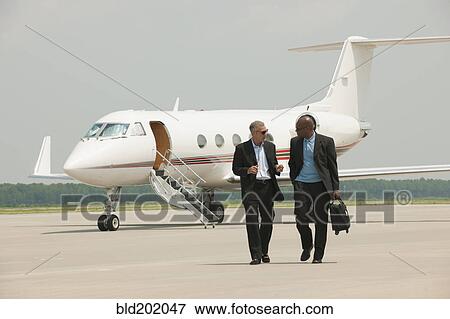 Businessmen walking on airport tarmac View Large Photo Image Stock Photo - Businessmen walking on airport tarmac. Fotosearch