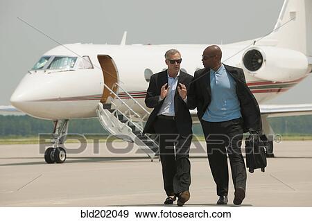 Stock Photo - Businessmen walking on airport tarmac. Fotosearch