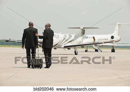 Stock Photograph - Businessmen walking on airport tarmac. Fotosearch