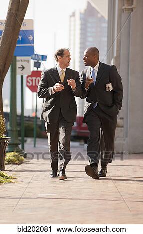 Stock Image - Businessmen walking together on city sidewalk. Fotosearch