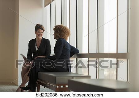 Stock Photograph - Businesswomen talking in waiting area. Fotosearch