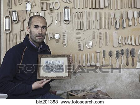 Stock Photo - Carpenter holding old photograph in workshop. Fotosearch