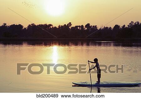 Stock Photo - Caucasian boy on paddleboard on lake. Fotosearch