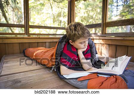 Stock Photo - Caucasian boy reading in sleeping bag. Fotosearch