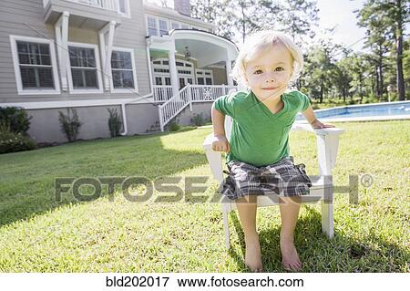Stock Photo - Caucasian boy sitting in chair in backyard. Fotosearch