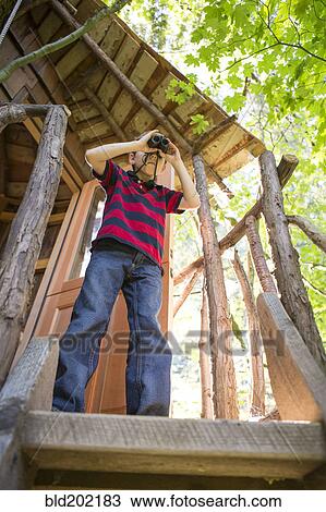 Stock Image - Caucasian boy using binoculars in tree house. Fotosearch
