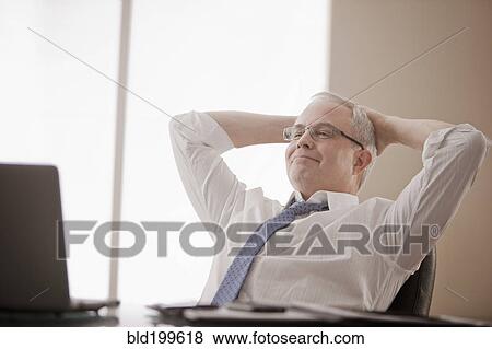 Caucasian businessman sitting at desk with hands on head View Large Photo Image Stock Photo - Caucasian businessman sitting at desk with hands on head. Fotosearch