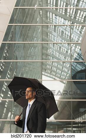 Stock Image - Caucasian businessman underneath umbrella. Fotosearch
