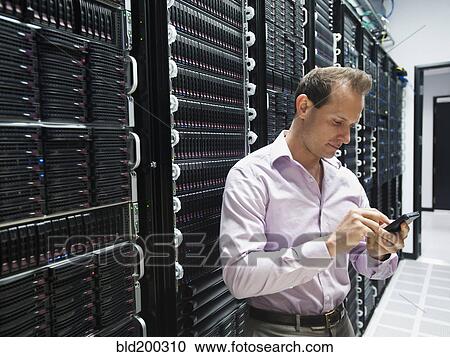 Stock Image - Caucasian businessman using cell phone in server room. Fotosearch