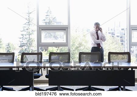 Stock Photograph - Caucasian businessman using cell phone in conference room. Fotosearch