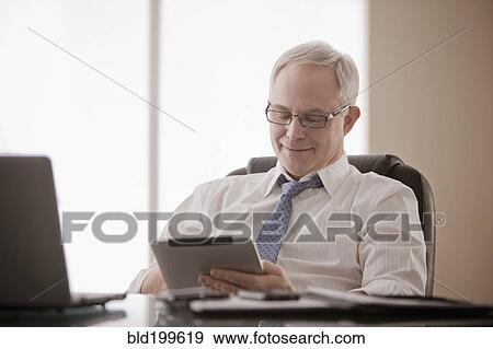 Stock Photo - Caucasian businessman using digital tablet at desk. Fotosearch