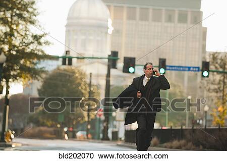 Stock Image - Caucasian businessman walking and talking on cell phone. Fotosearch