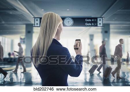 Stock Photograph - Caucasian businesswoman text messaging on cell phone in airport. Fotosearch