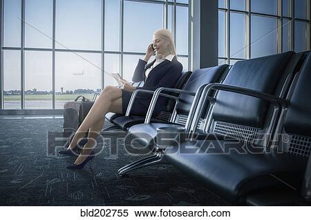 Stock Photography - Caucasian businesswoman using cell phone and digital tablet in airport. Fotosearch