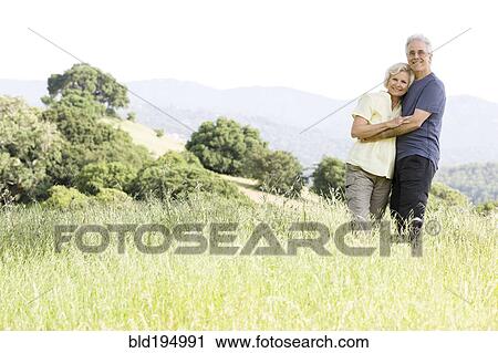 Stock Image - Caucasian couple hugging in field. Fotosearch