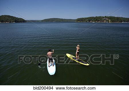 Caucasian couple on paddle boards on lake View Large Photo Image Picture - Caucasian couple on paddle boards on lake. Fotosearch