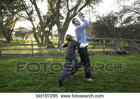 Stock Photography - Caucasian father and sons playing football in yard. Fotosearch
