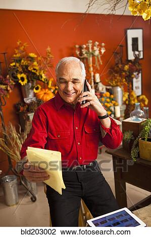 Stock Image - Caucasian florist talking on phone in shop. Fotosearch
