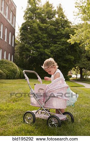 Stock Image - Caucasian girl dressed as princess playing with stroller. Fotosearch