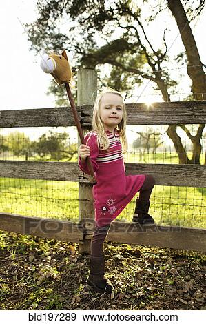 Stock Photo - Caucasian girl holding stick horse near fence. Fotosearch