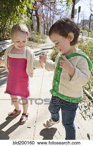 Stock Image - Caucasian girls holding hands on sidewalk. Fotosearch