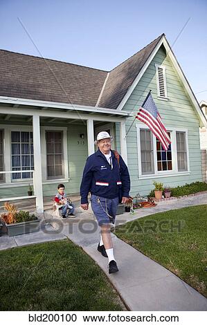 Stock Image - Caucasian mailman walking in front yard. Fotosearch