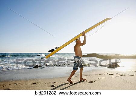Stock Image - Caucasian man carrying paddleboard. Fotosearch
