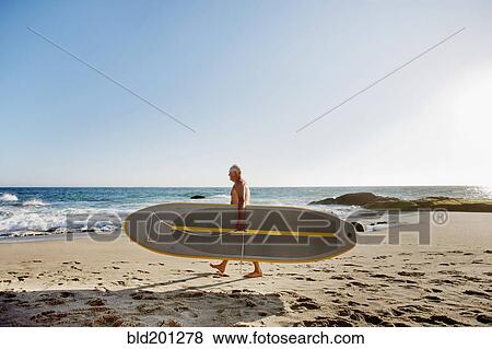 Stock Photo - Caucasian man carrying paddleboard. Fotosearch