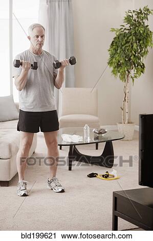 Stock Image - Caucasian man exercising in living room. Fotosearch