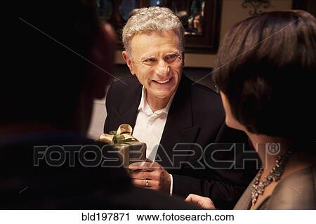 Stock Image - Caucasian man giving woman gift in restaurant. Fotosearch