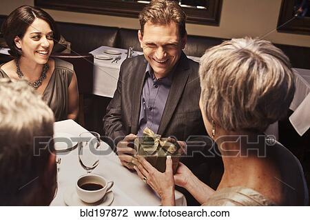 Stock Image - Caucasian man giving woman gift in restaurant. Fotosearch