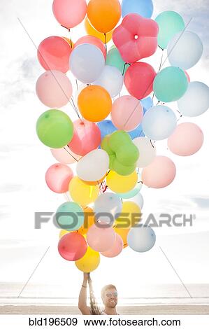Stock Photo - Caucasian man holding balloons on beach. Fotosearch
