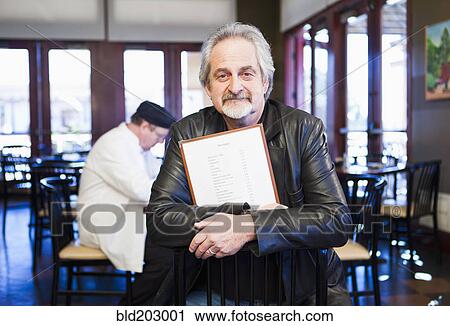 Stock Image - Caucasian man holding menu in restaurant. Fotosearch