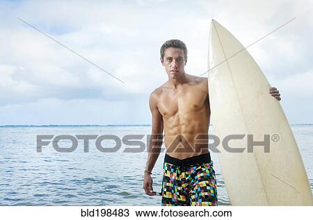 Stock Image - Caucasian man holding surfboard near ocean. Fotosearch