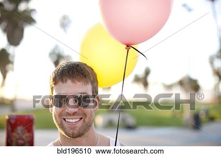 Stock Image - Caucasian man holding two balloons. Fotosearch