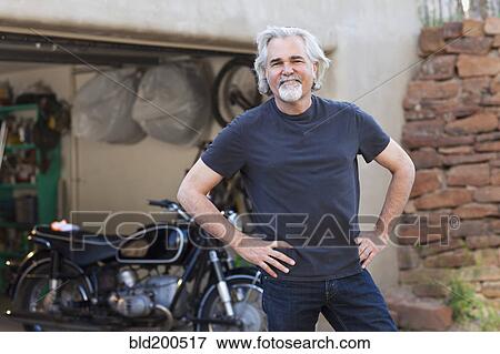 Stock Photo - Caucasian man in driveway with motorcycle. Fotosearch
