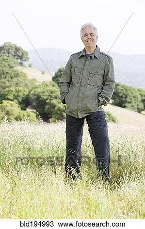 Stock Image - Caucasian man in field with hands in pockets. Fotosearch