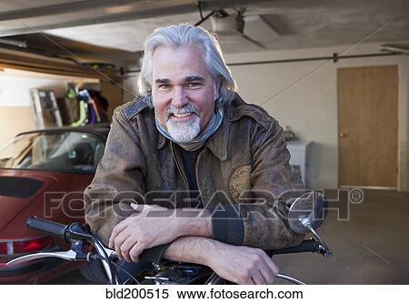 Stock Photography - Caucasian man in garage with motorcycle. Fotosearch