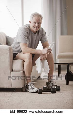 Stock Image - Caucasian man in living room drinking water after exercise. Fotosearch