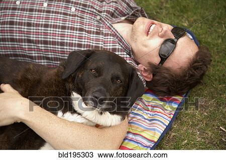 Stock Image - Caucasian man laying in park with dog. Fotosearch