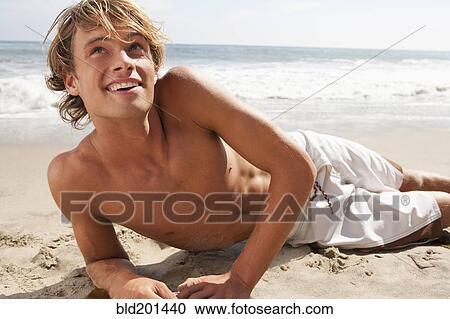 Stock Image - Caucasian man laying on beach. Fotosearch