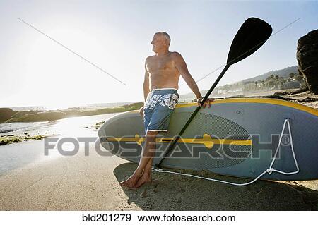 Stock Photo - Caucasian man leaning on paddleboard. Fotosearch