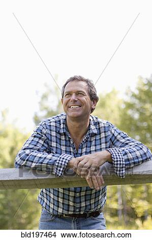 Picture - Caucasian man leaning on wooden fence. Fotosearch