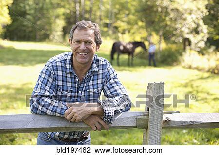 Stock Image - Caucasian man leaning on wooden fence. Fotosearch