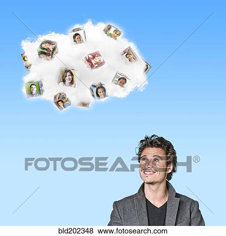 Stock Photo - Caucasian man looking at cloud containing cubes with pictures of people. Fotosearch