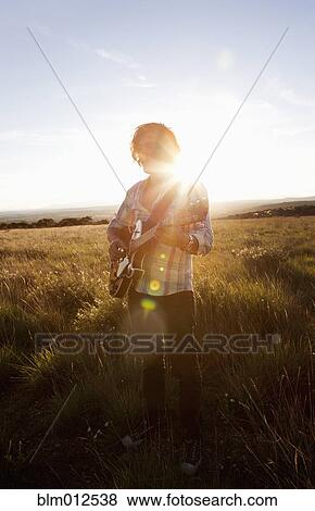 Stock Photo - Caucasian man playing guitar in field. Fotosearch