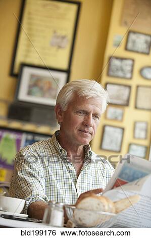 Stock Photograph - Caucasian man reading newspaper in restaurant. Fotosearch